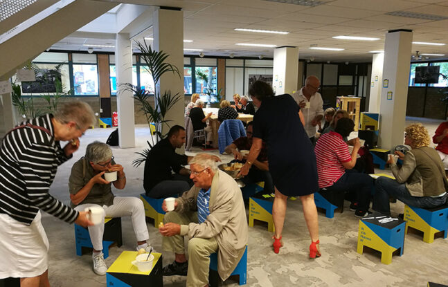 Een groep van ongeveer 20 mensen zitten in een aula bij elkaar en overleggen in kleine groepjes met elkaar